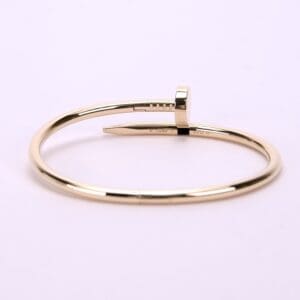 Gold nail-shaped bangle on pink background.