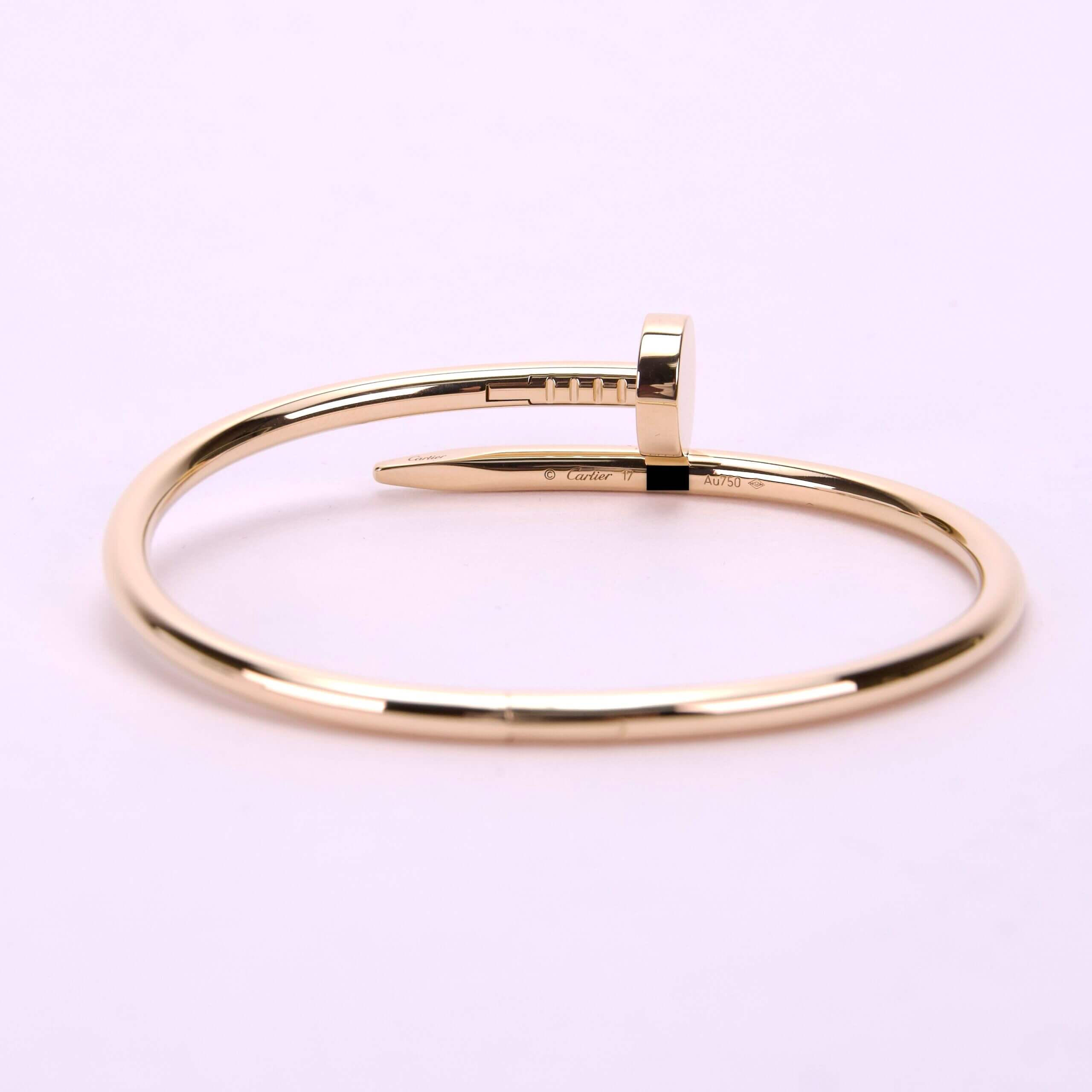 Gold nail-shaped bangle on pink background.
