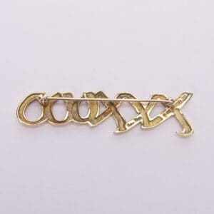 Gold brooch with intricate lettering design.