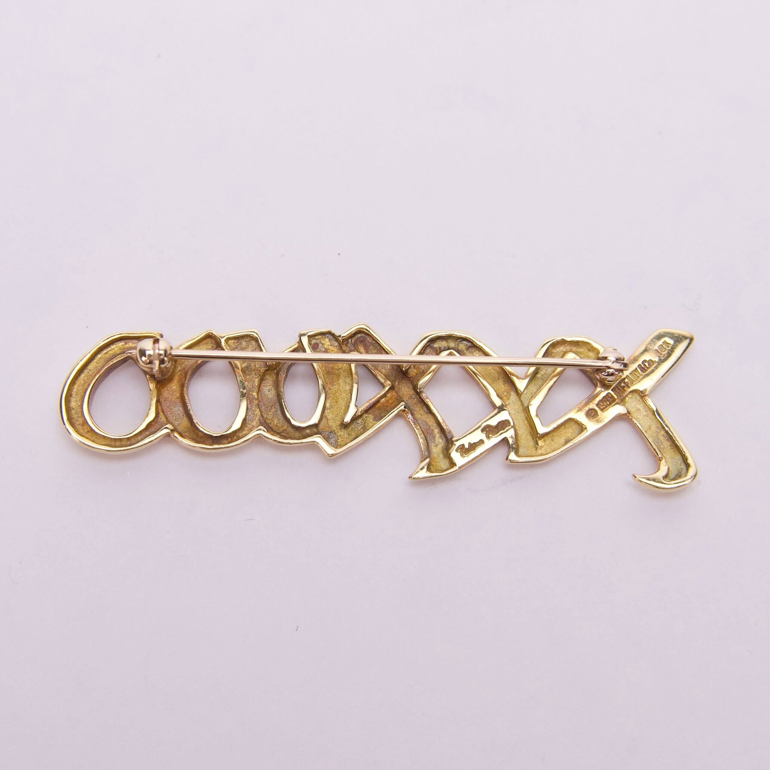 Gold brooch with intricate lettering design.