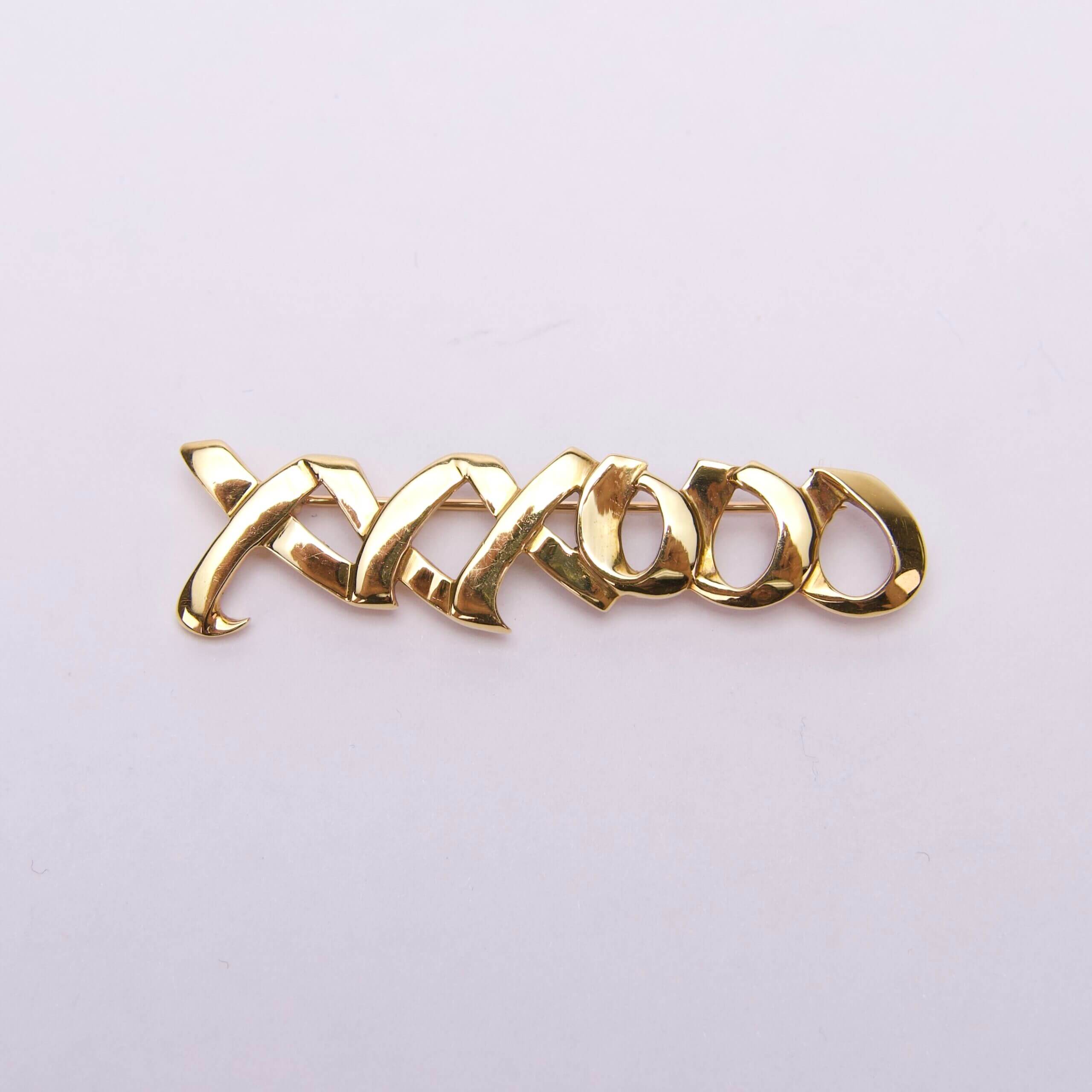 Gold-plated "XOXO" brooch on white background.