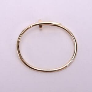 Gold nail-shaped bangle on white background.