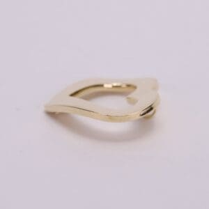 Gold, abstract-shaped metal clip on surface.