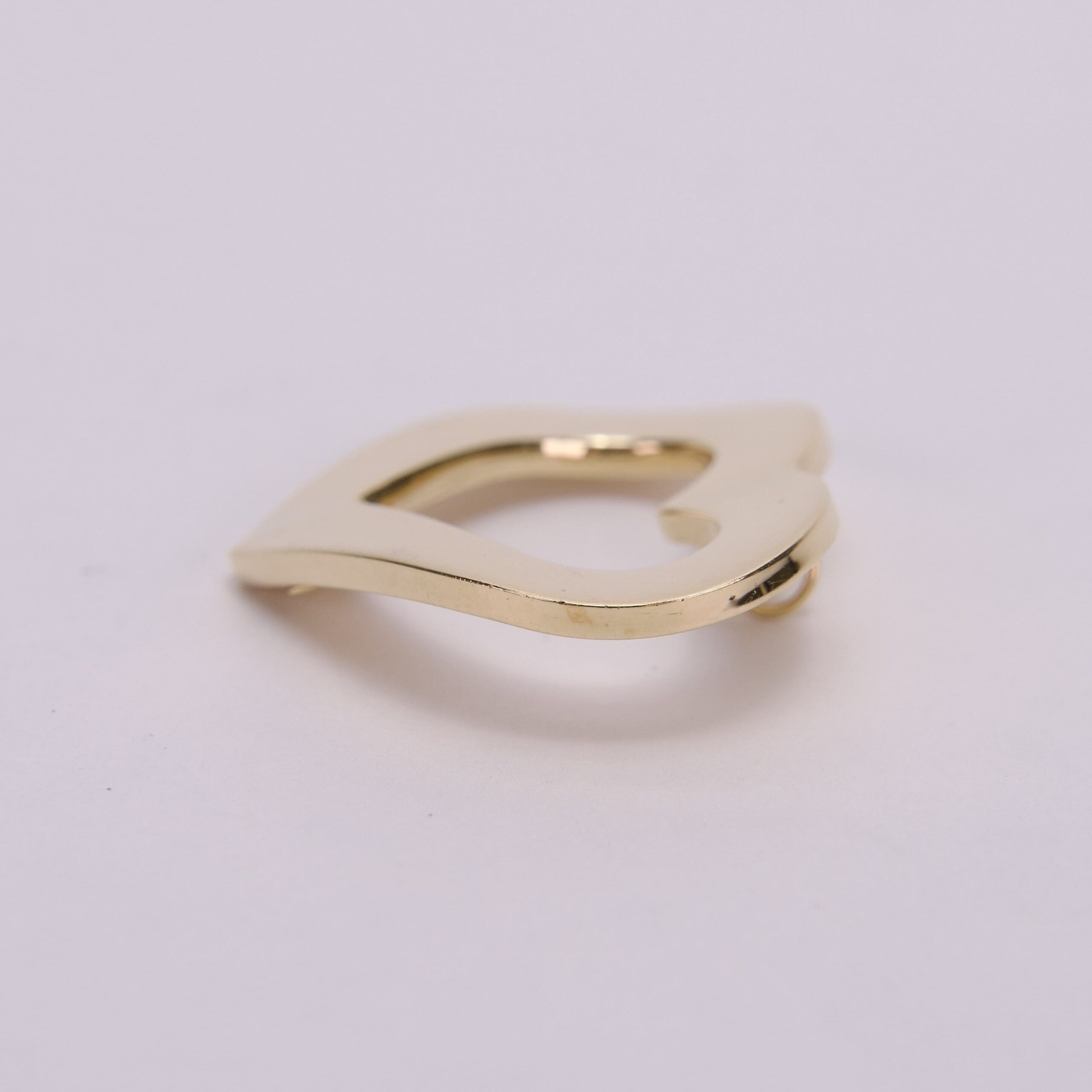 Gold, abstract-shaped metal clip on surface.