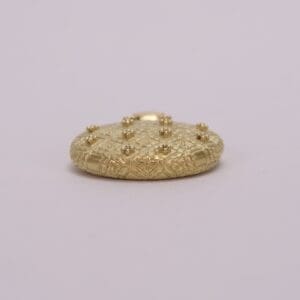 Gold textured button with raised embellishments.