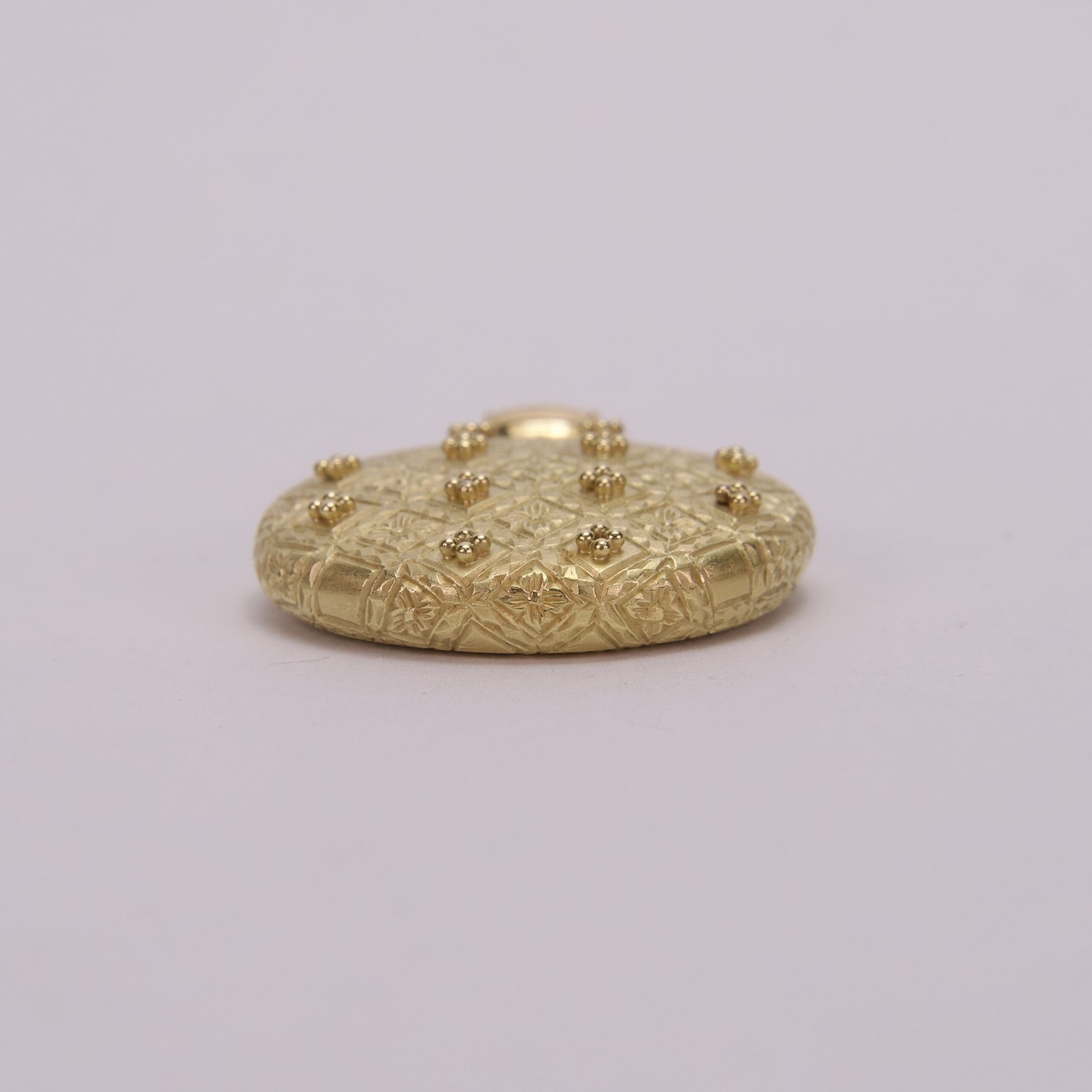 Gold textured button with raised embellishments.
