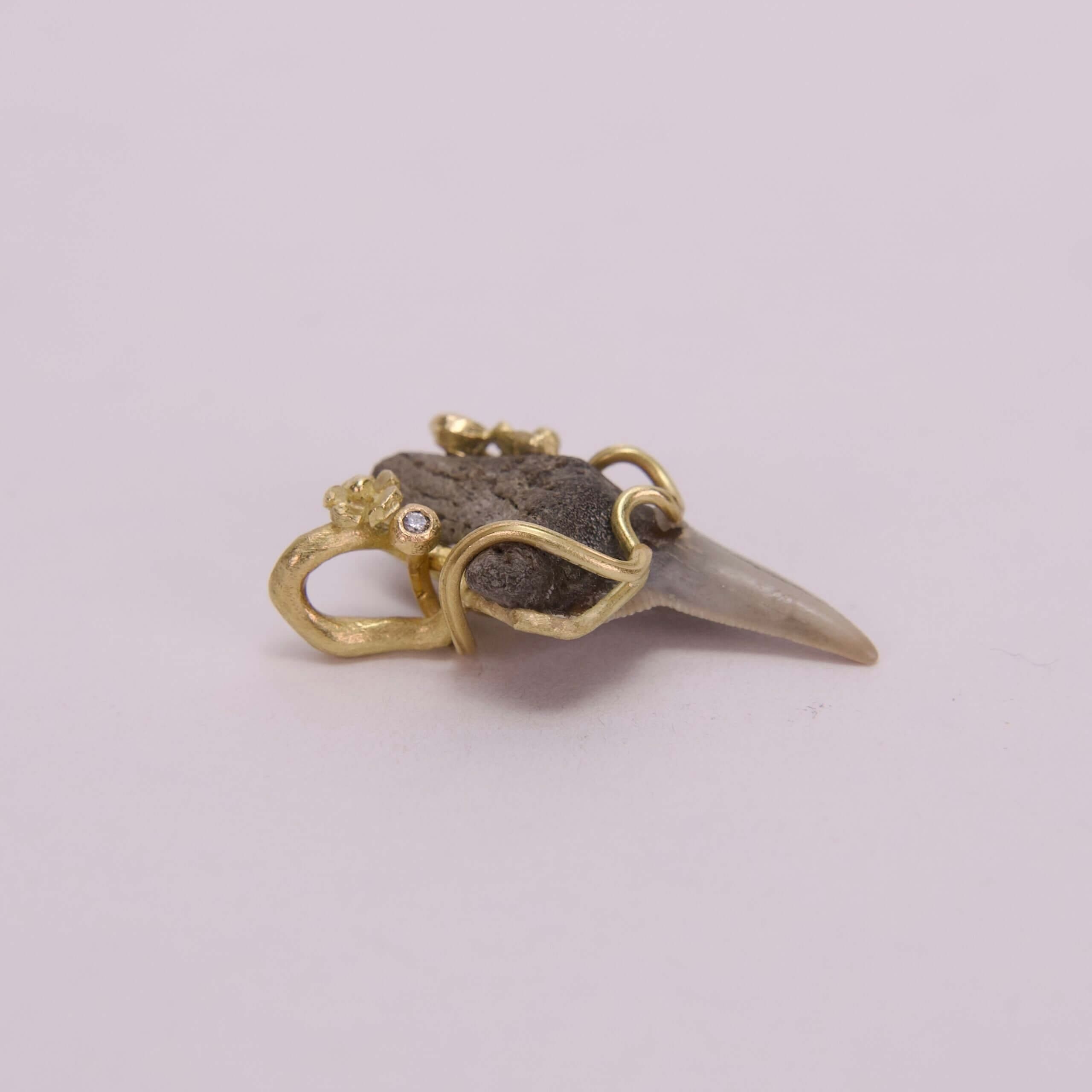 Gold-wrapped fossil tooth pendant with gemstone.