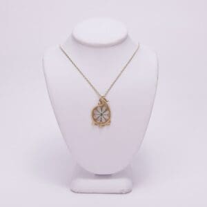 Gold pendant necklace on white display stand.