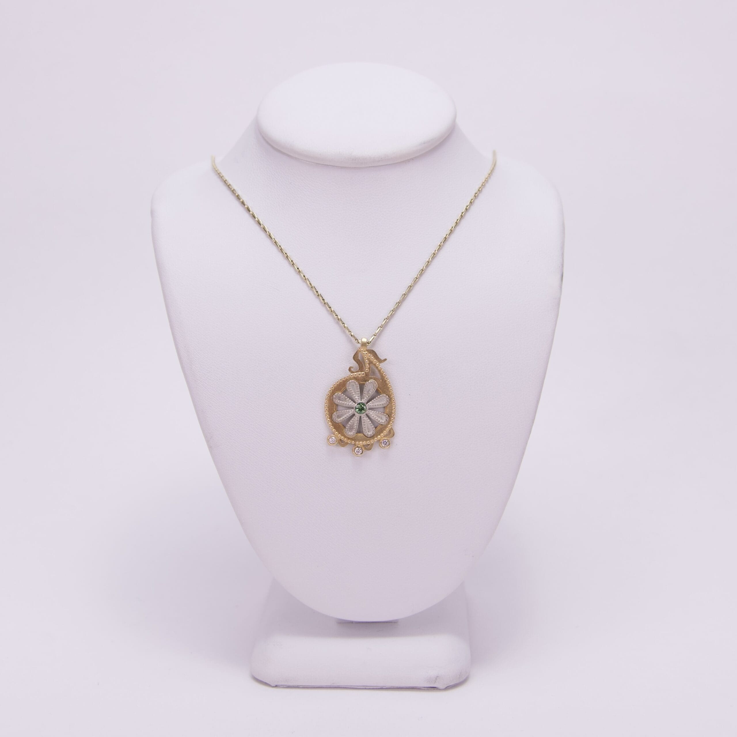 Gold pendant necklace on white display stand.