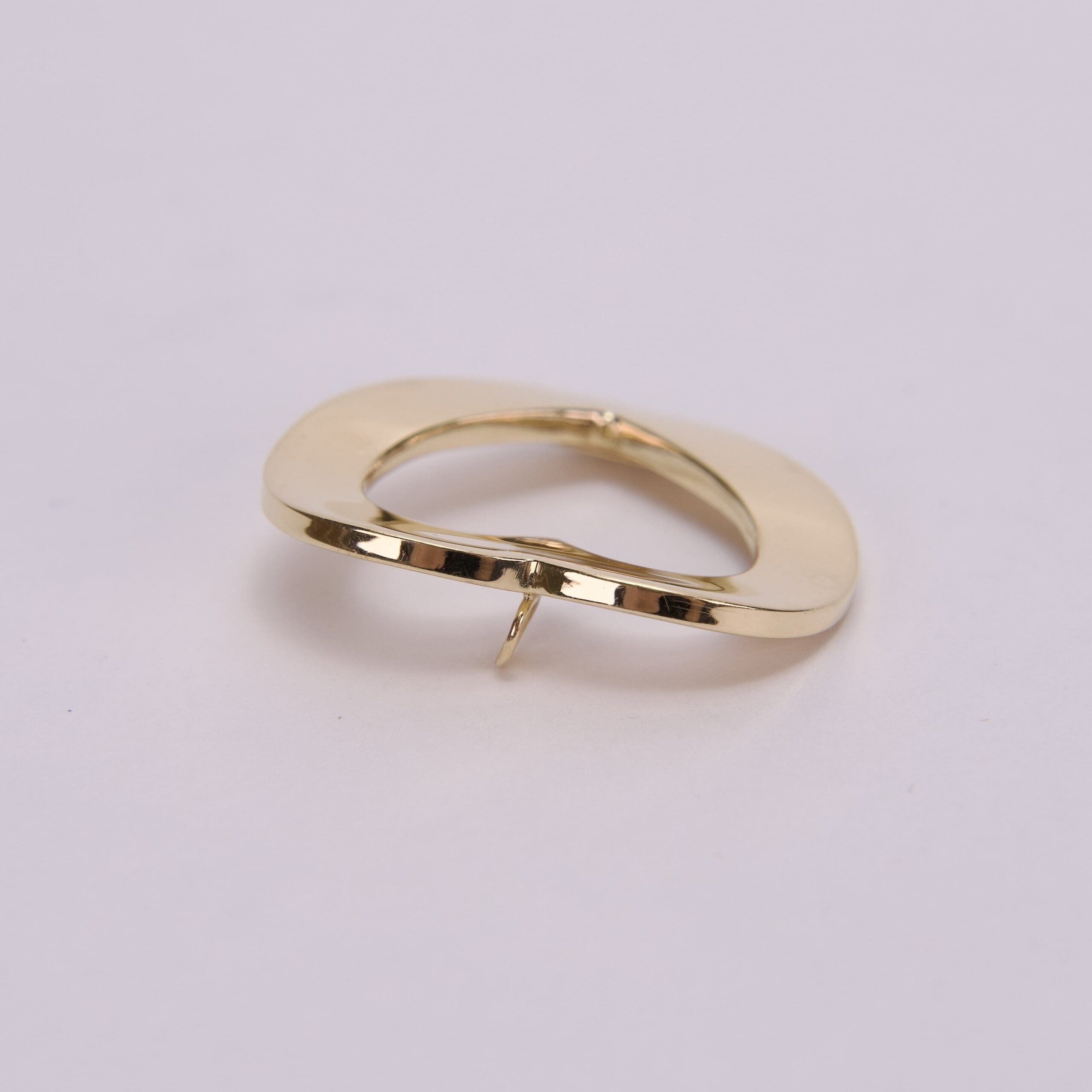 Gold abstract-shaped brooch on pink background.