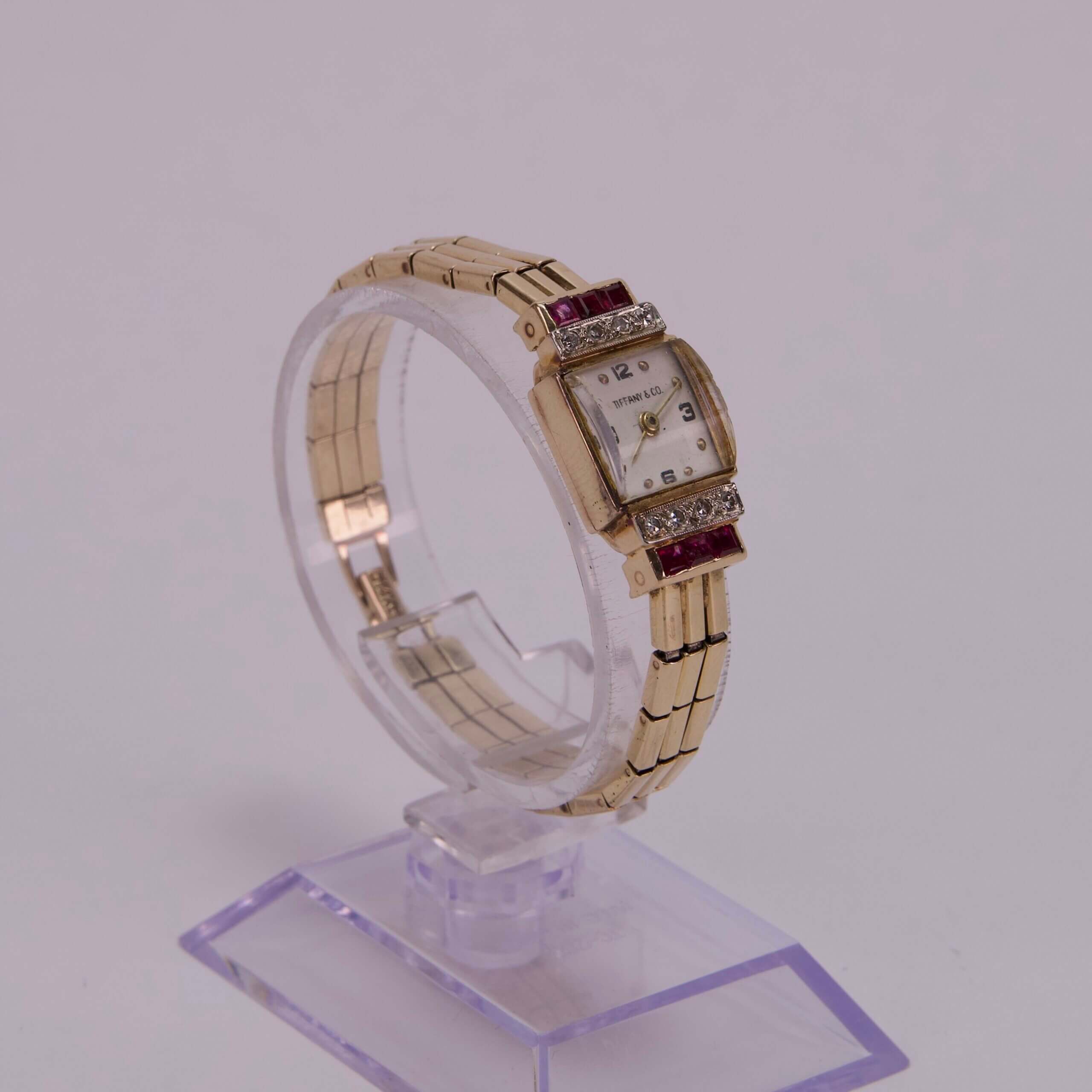 Gold wristwatch with jeweled accents on stand.