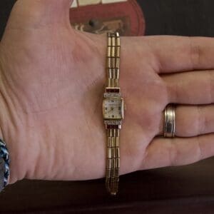 Hand holding a small vintage gold watch.