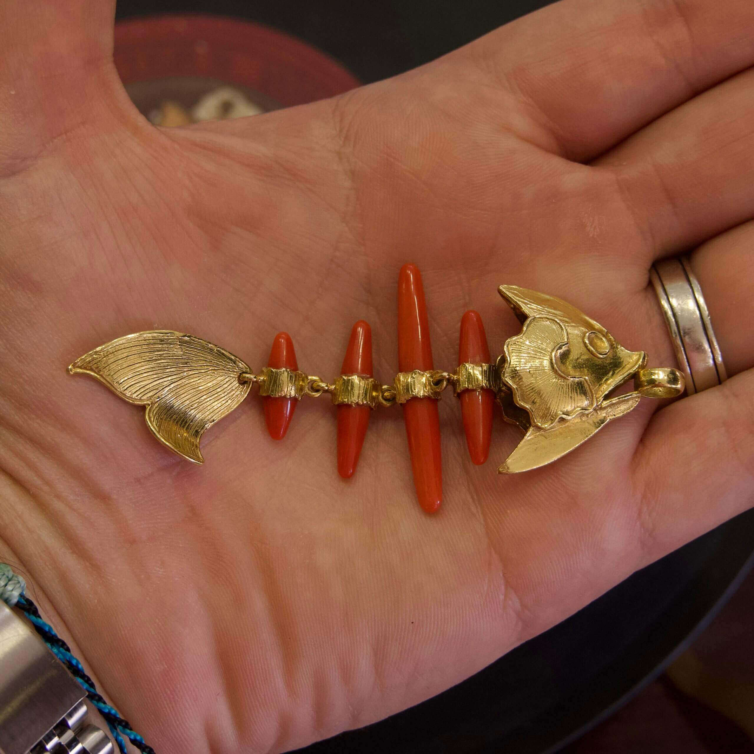 Gold and red fishbone pendant in hand.