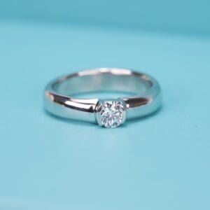 Silver ring with center diamond on turquoise background.