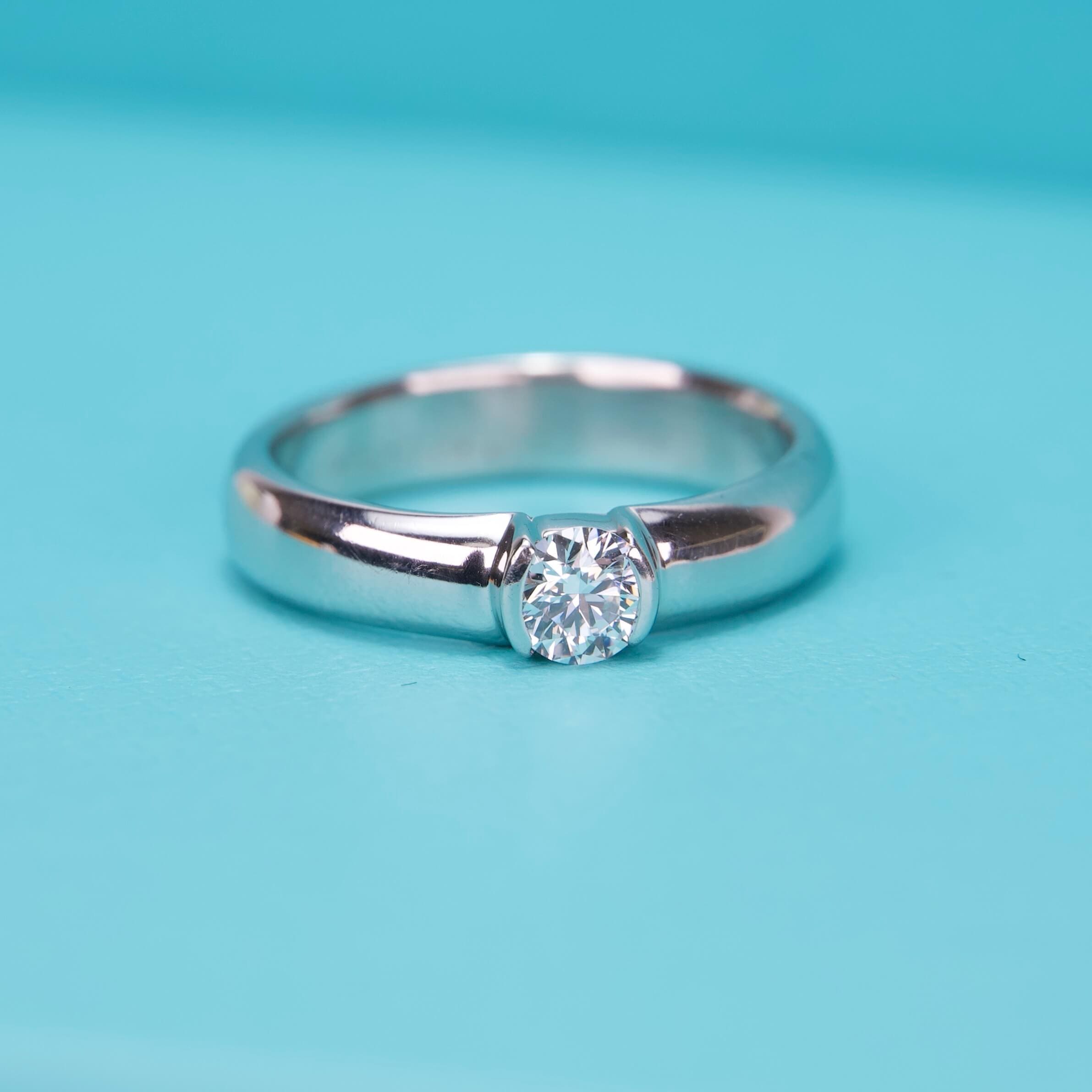 Silver ring with center diamond on turquoise background.