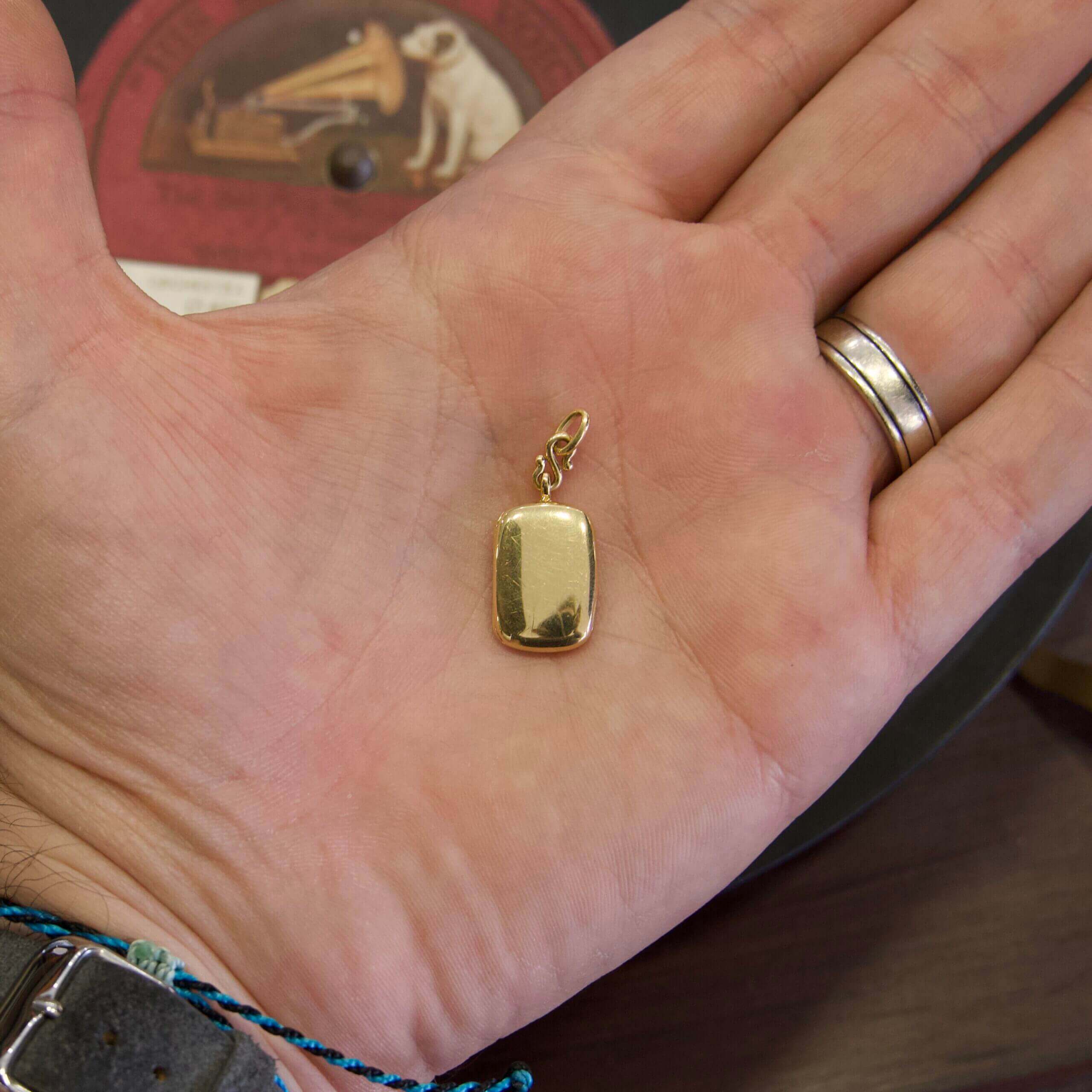 Hand holding a small gold pendant.