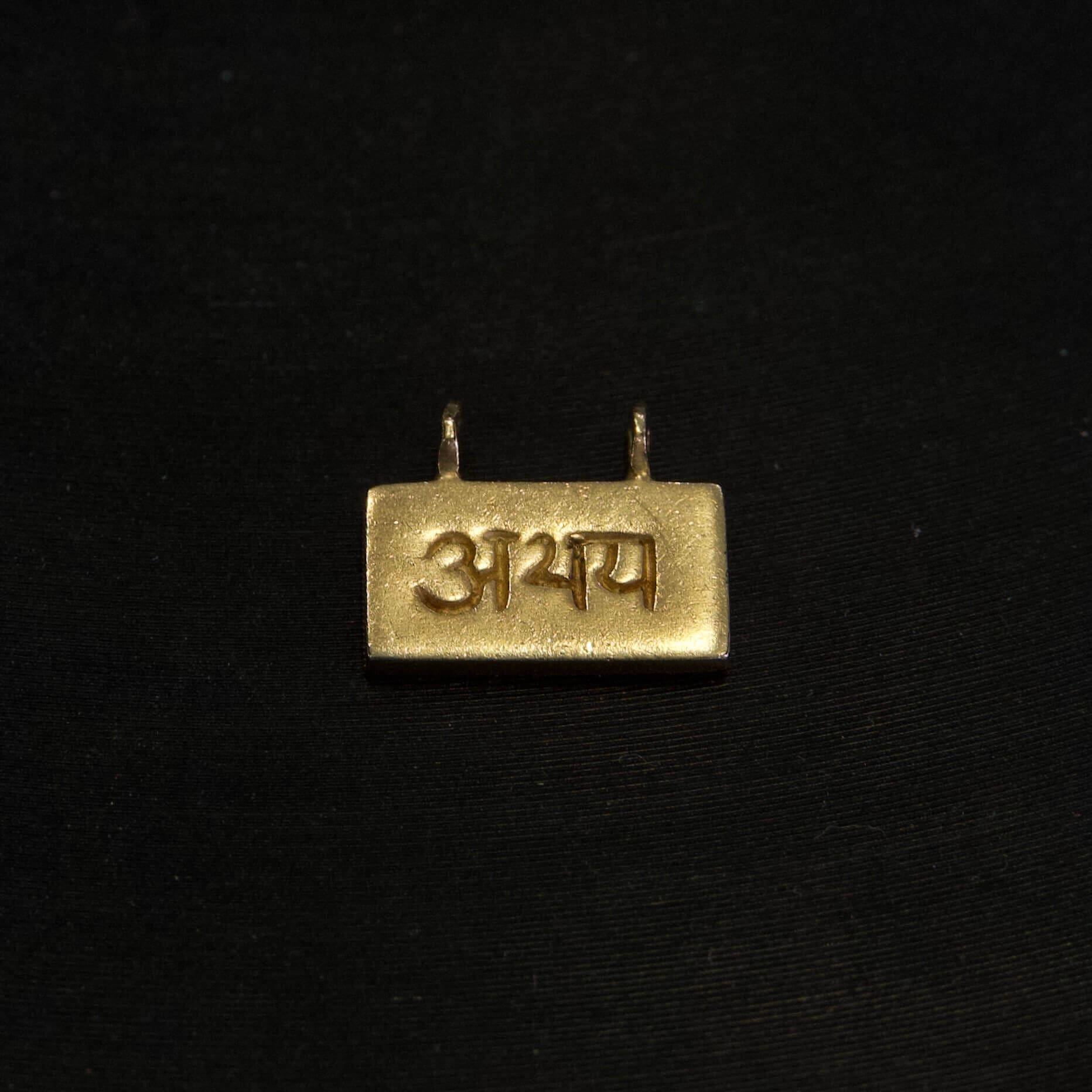Gold pendant with Hindi script on black.