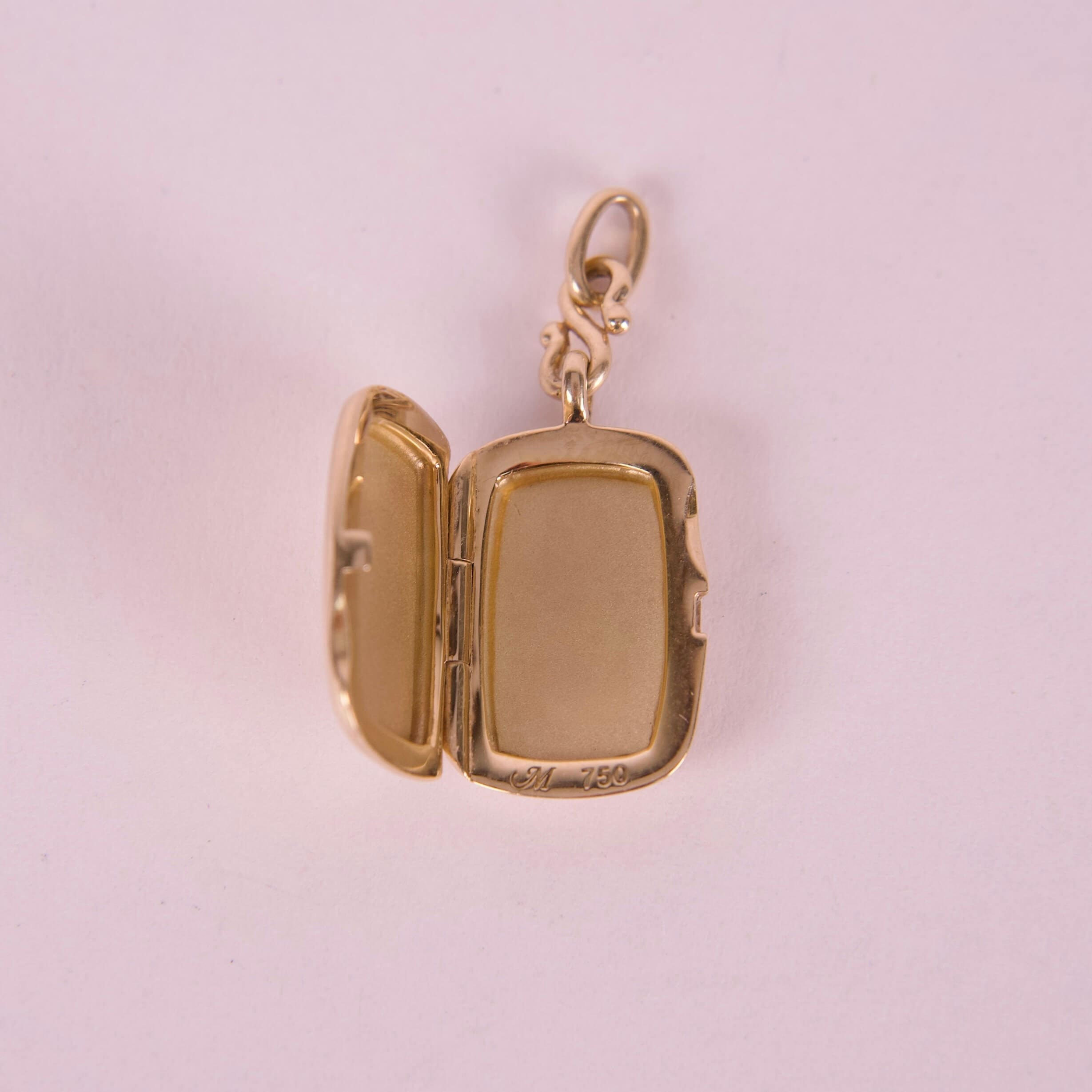 Gold locket with open compartment on pink background.