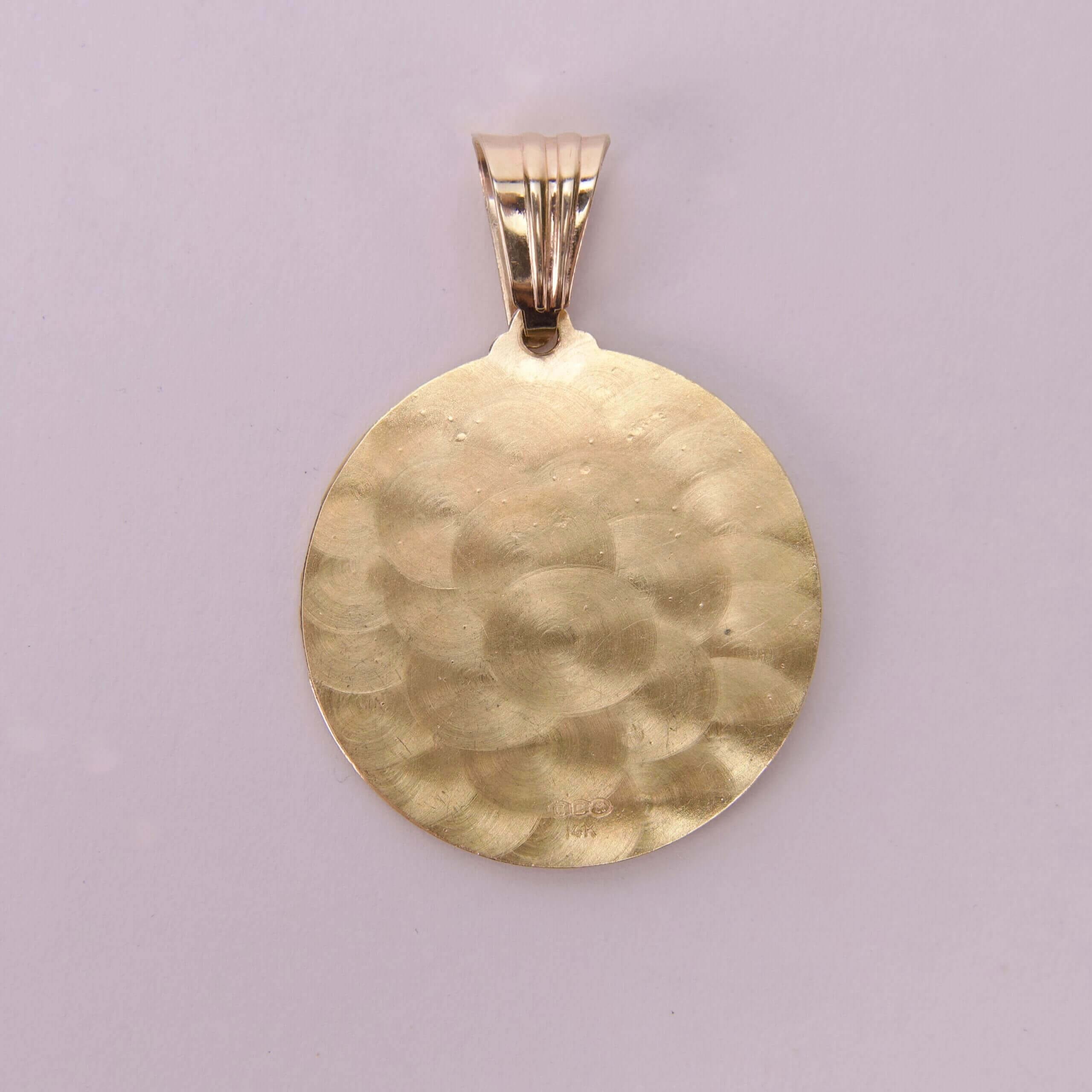 Gold textured round pendant on pink background.