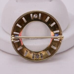 Gold circular brooch with gemstone accents.