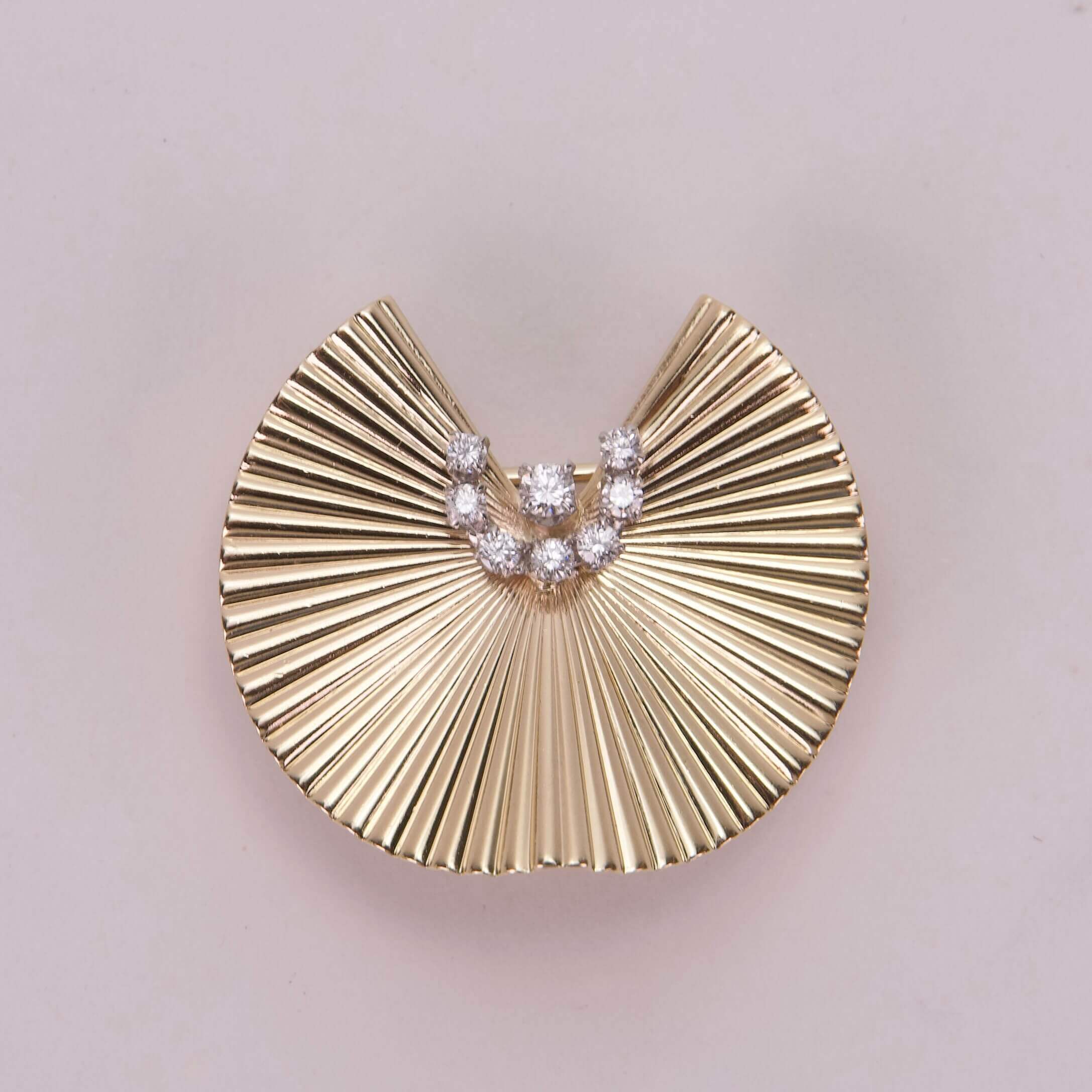 Gold fan-shaped brooch with diamond accents.