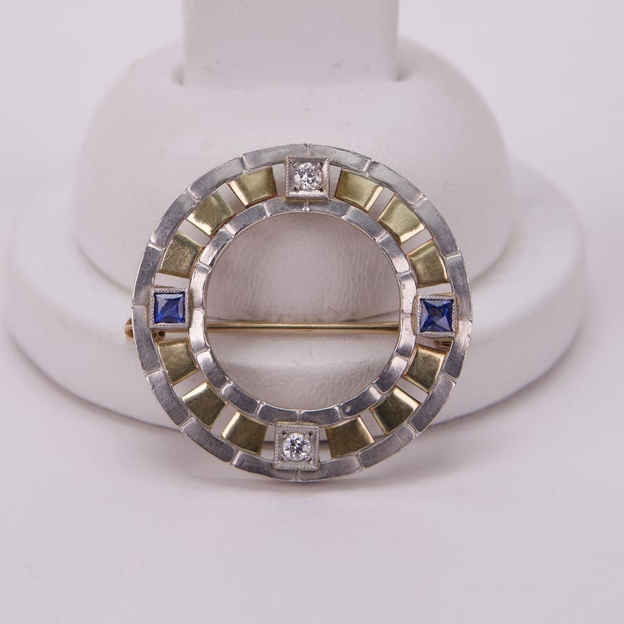Circular brooch with blue and clear gems.
