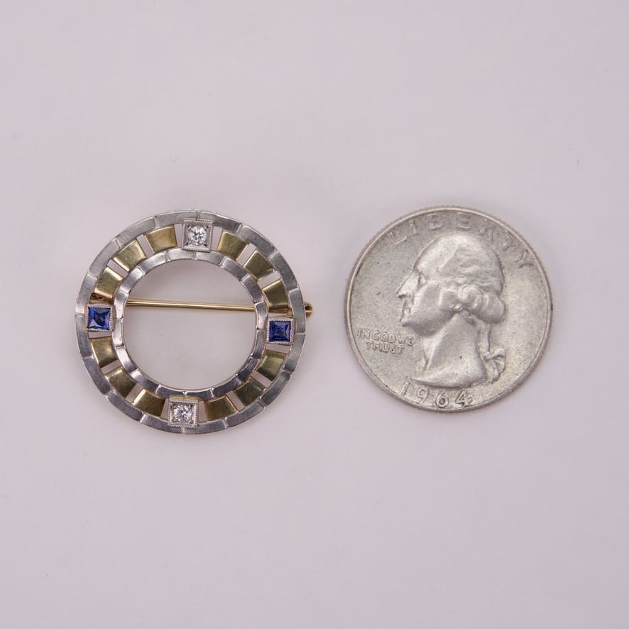 Circular brooch beside a U.S. quarter.