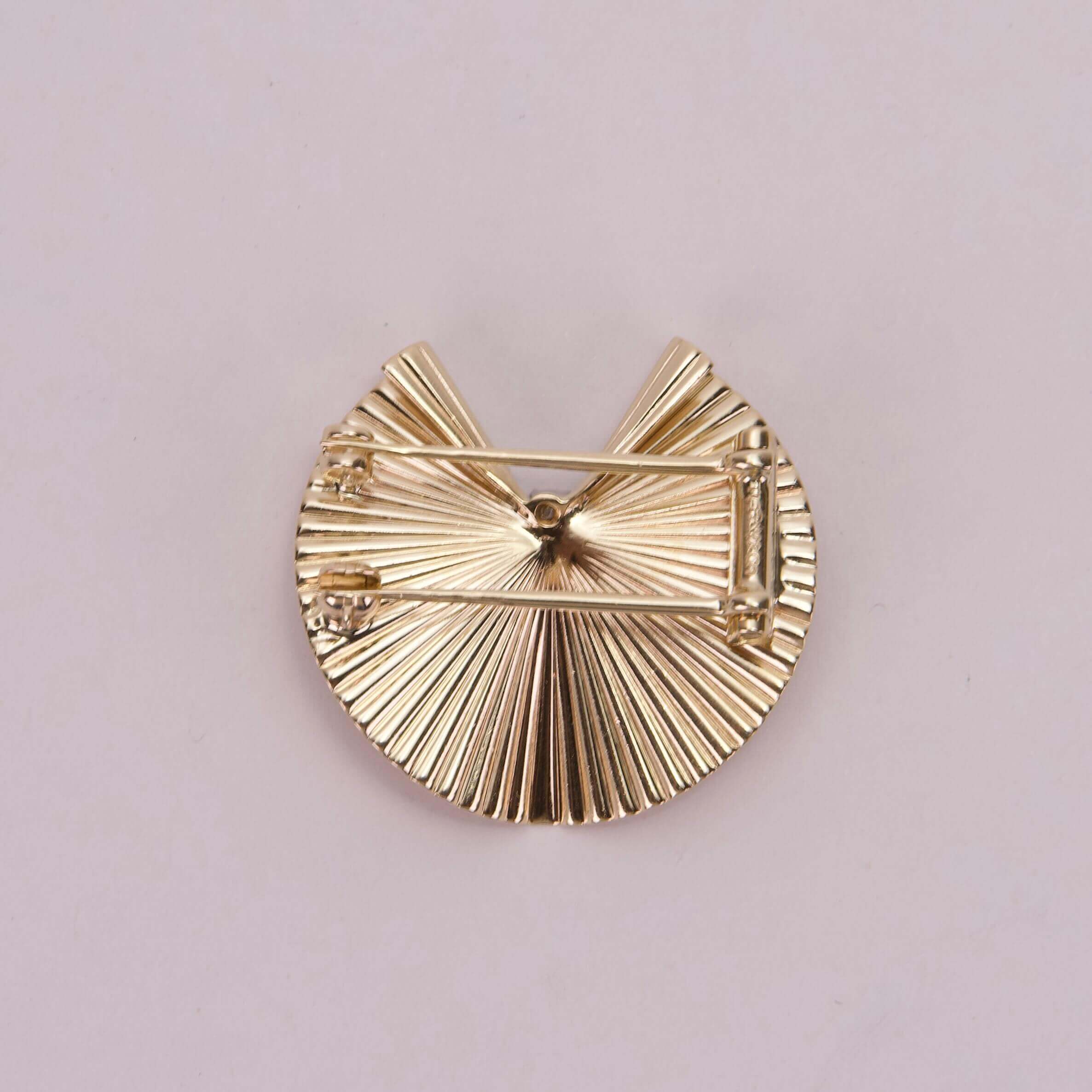 Gold circular brooch with textured design.
