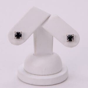 Black stud earrings on white display stand.