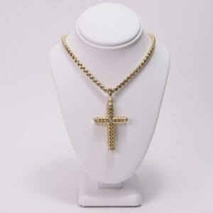 Gold cross necklace on display stand.