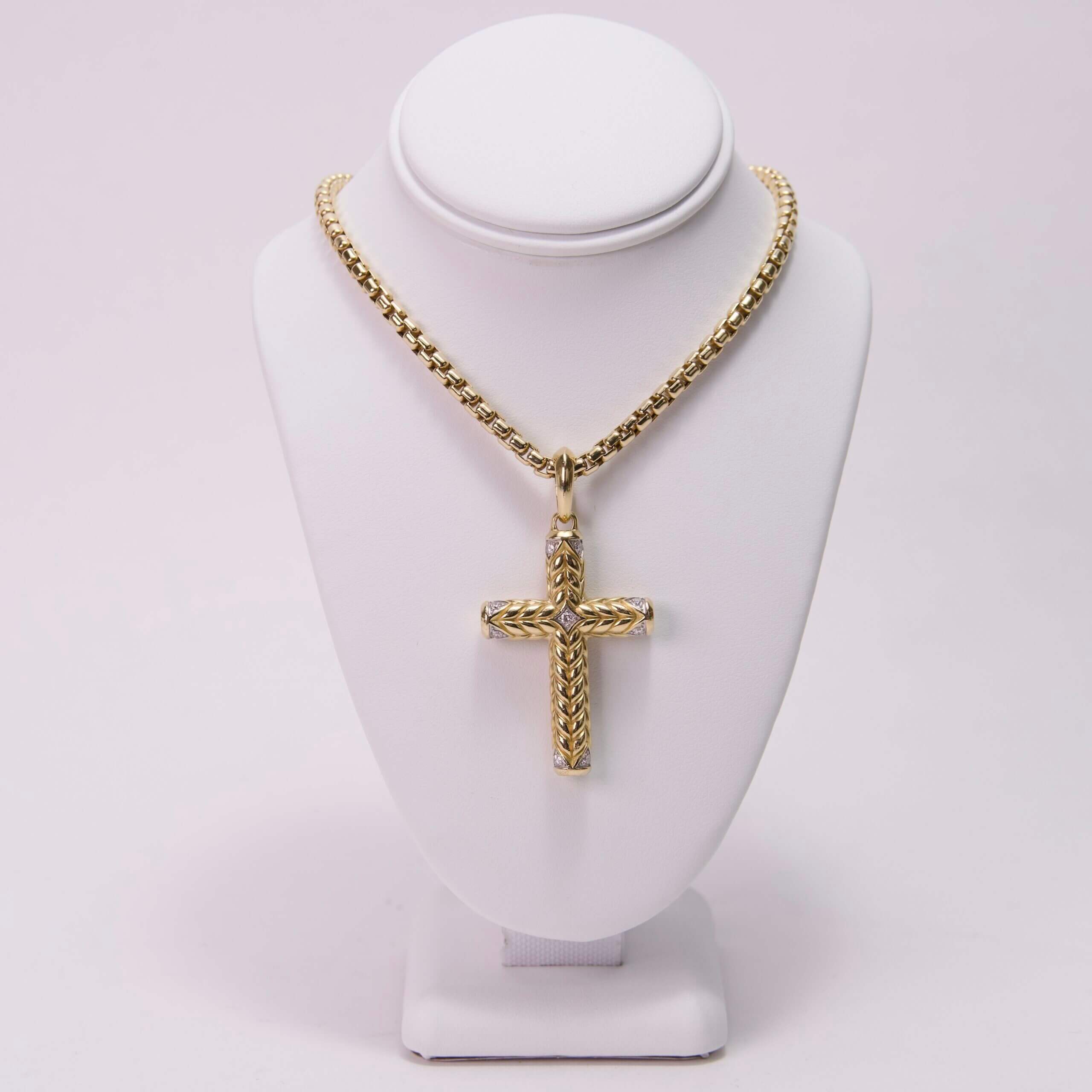 Gold cross necklace on display stand.
