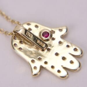 Gold pendant with red gemstone and dots.