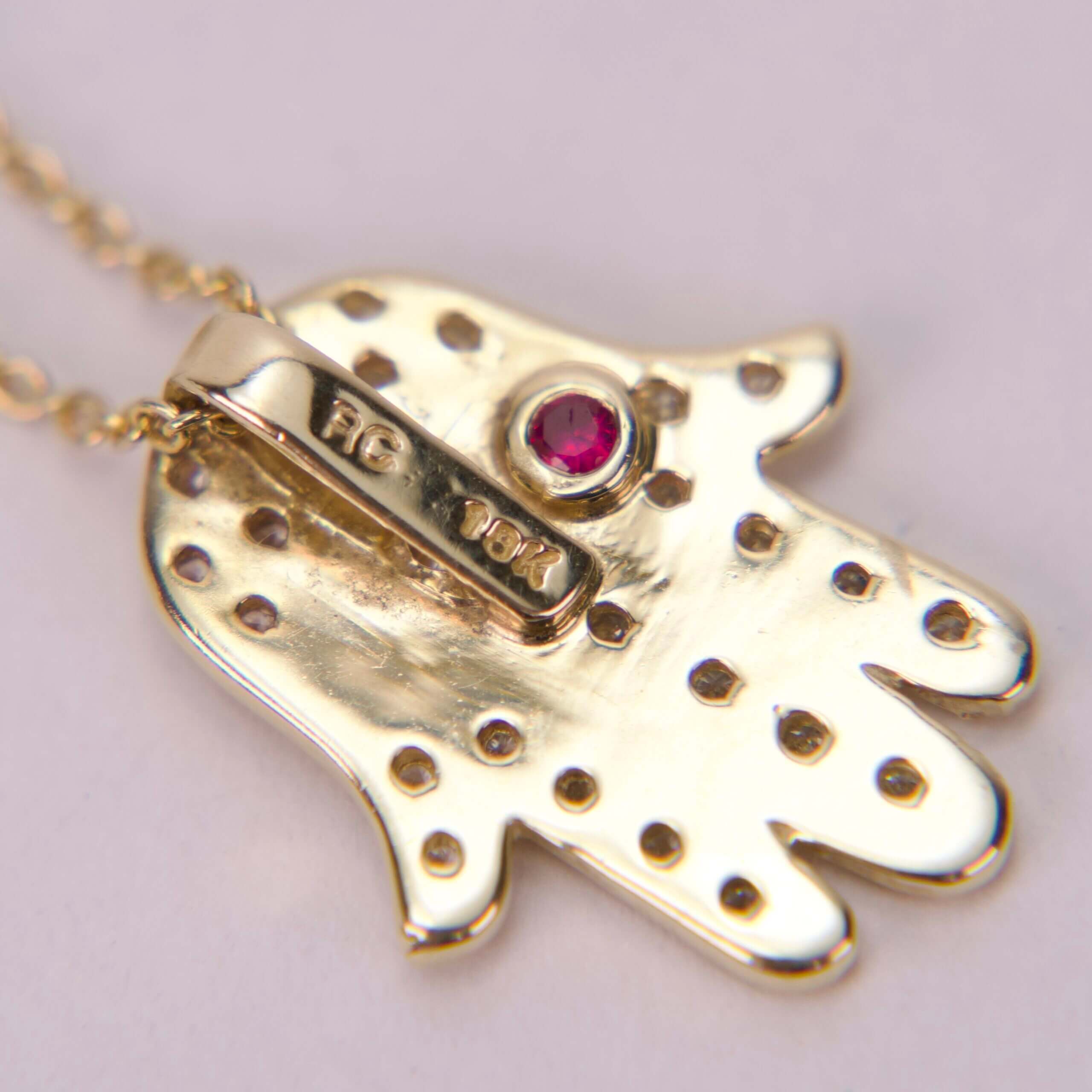 Gold pendant with red gemstone and dots.