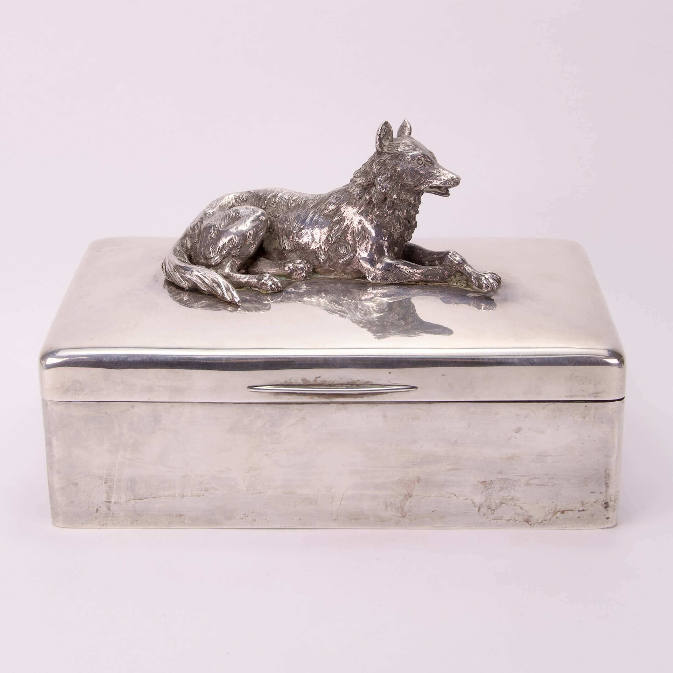 Silver box with wolf figurine on top.