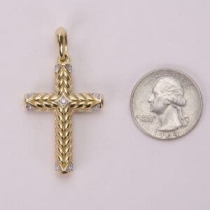 Gold cross pendant beside a quarter coin.