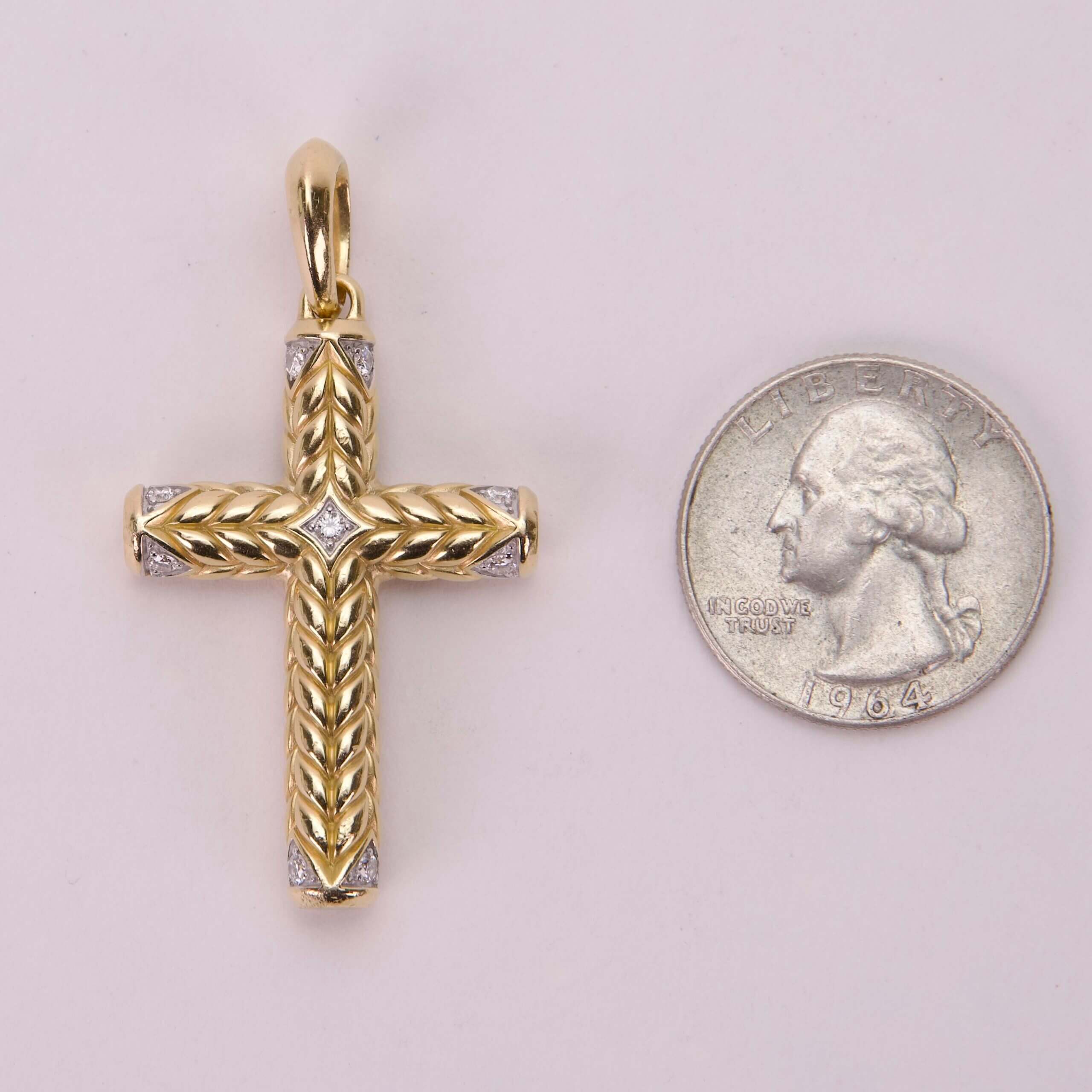 Gold cross pendant beside a quarter coin.