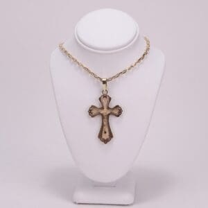 Gold cross necklace on display stand.