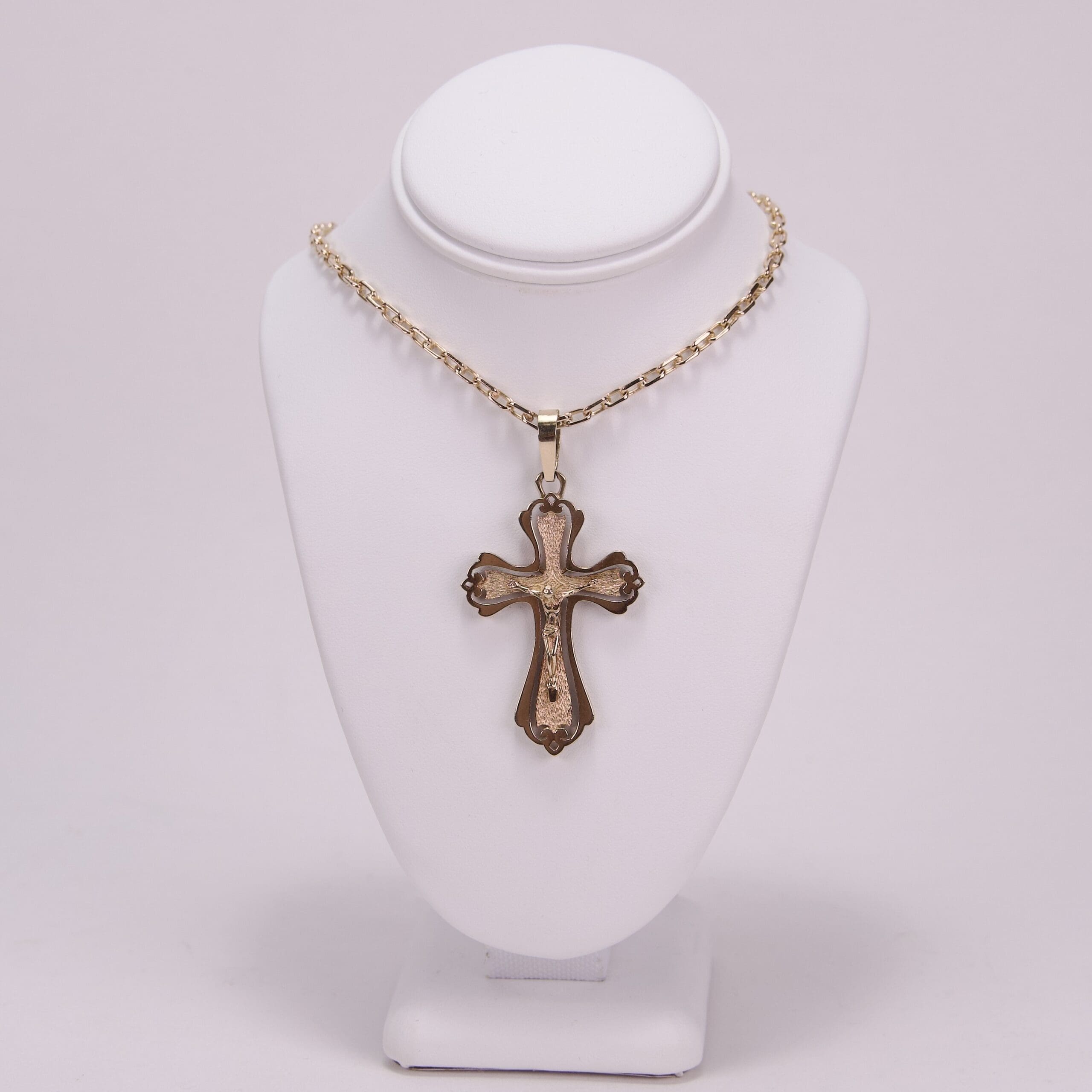 Gold cross necklace on display stand.