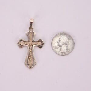 Gold cross pendant beside a silver coin.