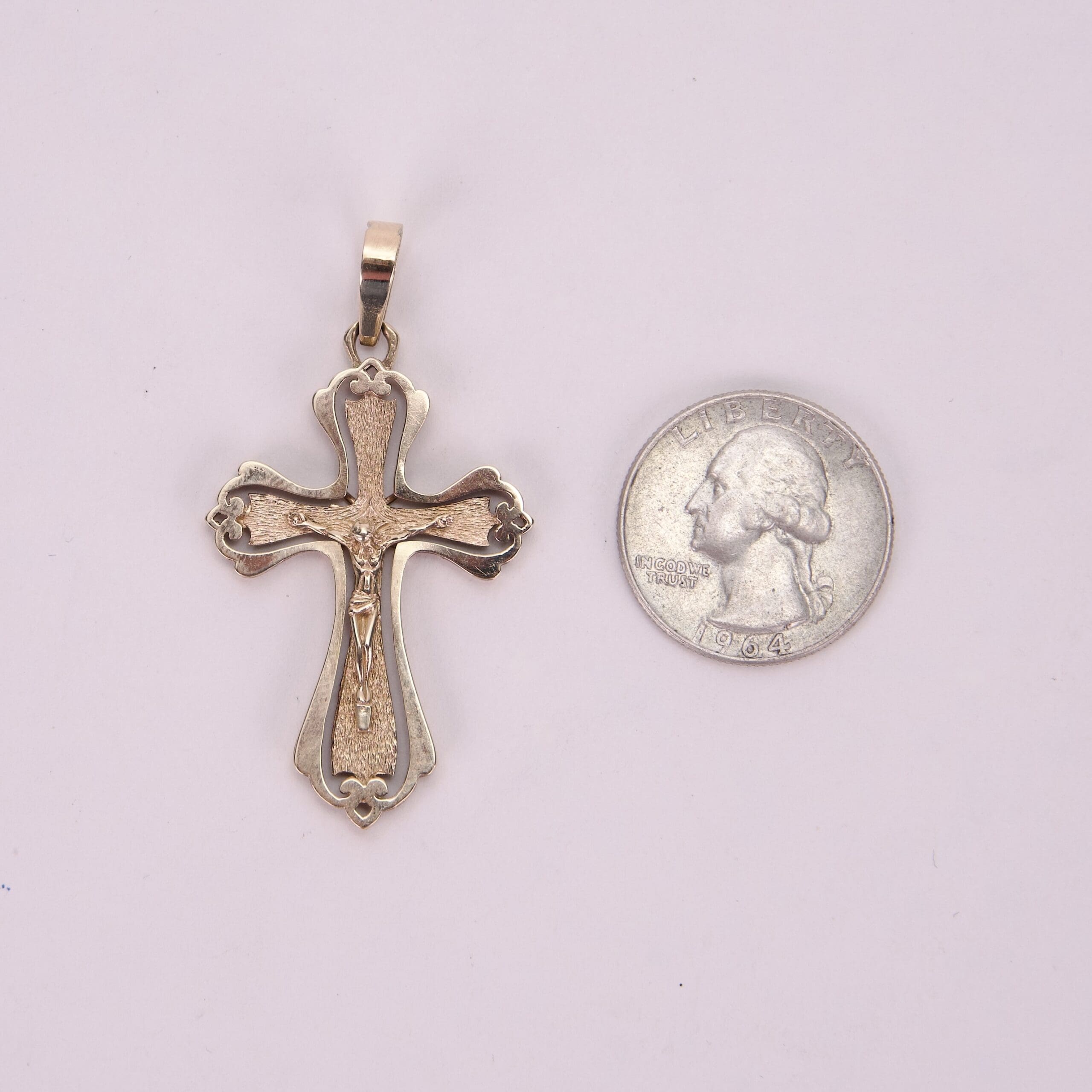 Gold cross pendant beside a silver coin.