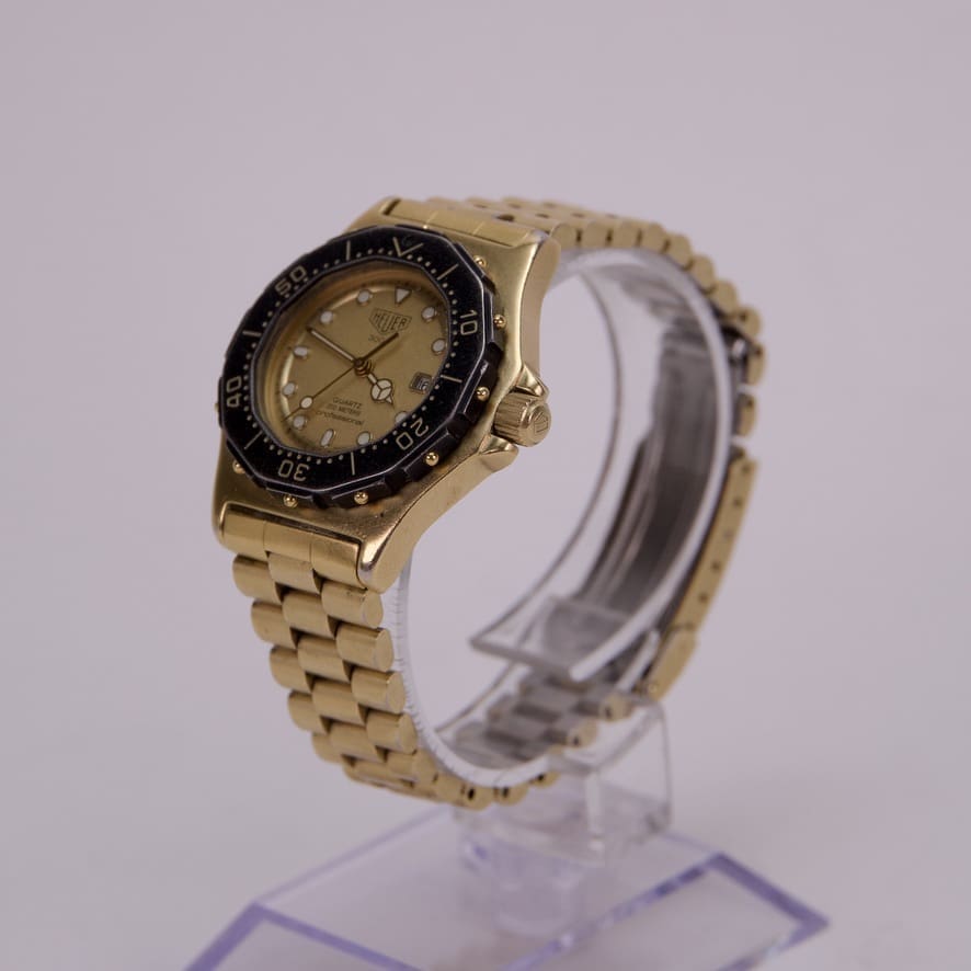 Gold wristwatch with black bezel on stand.