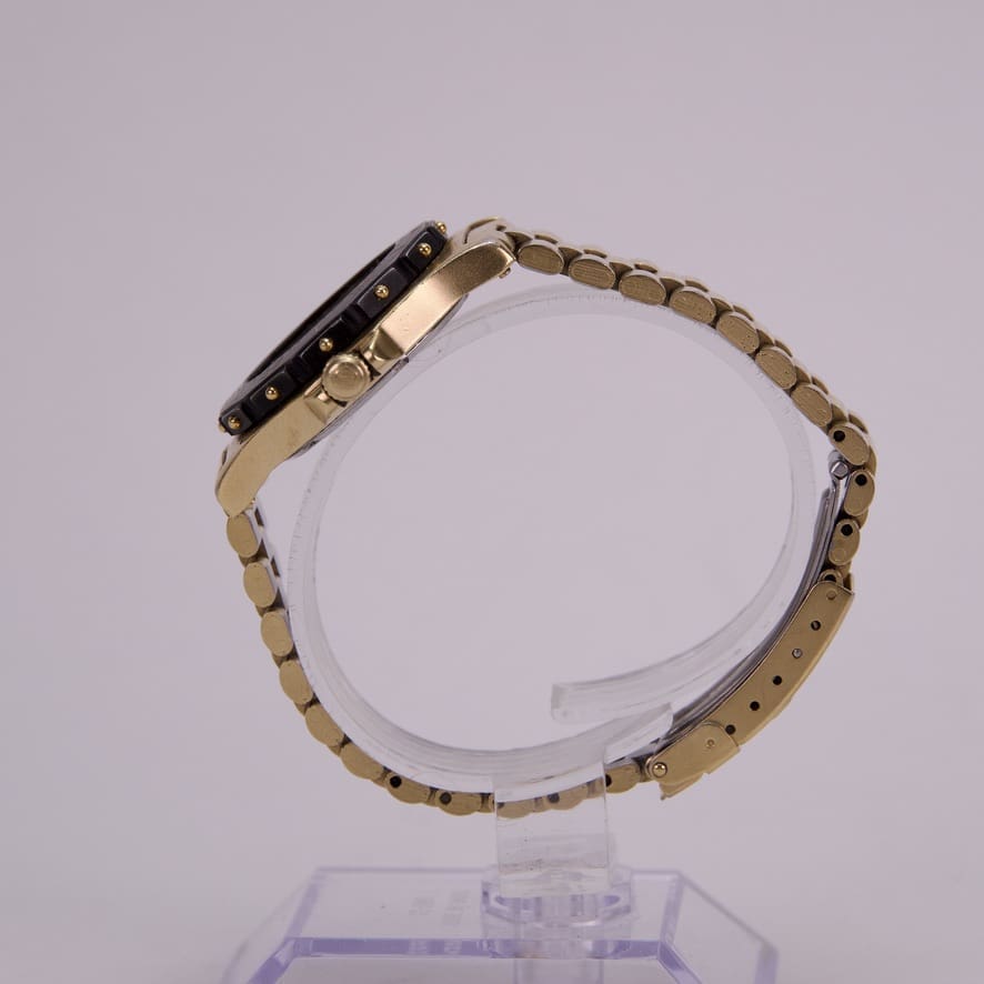 Gold wristwatch on transparent display stand.
