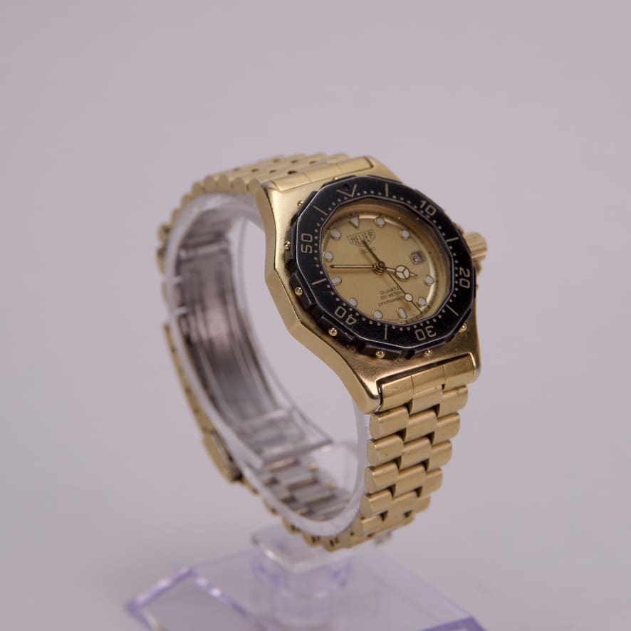 Gold wristwatch with black bezel on stand.
