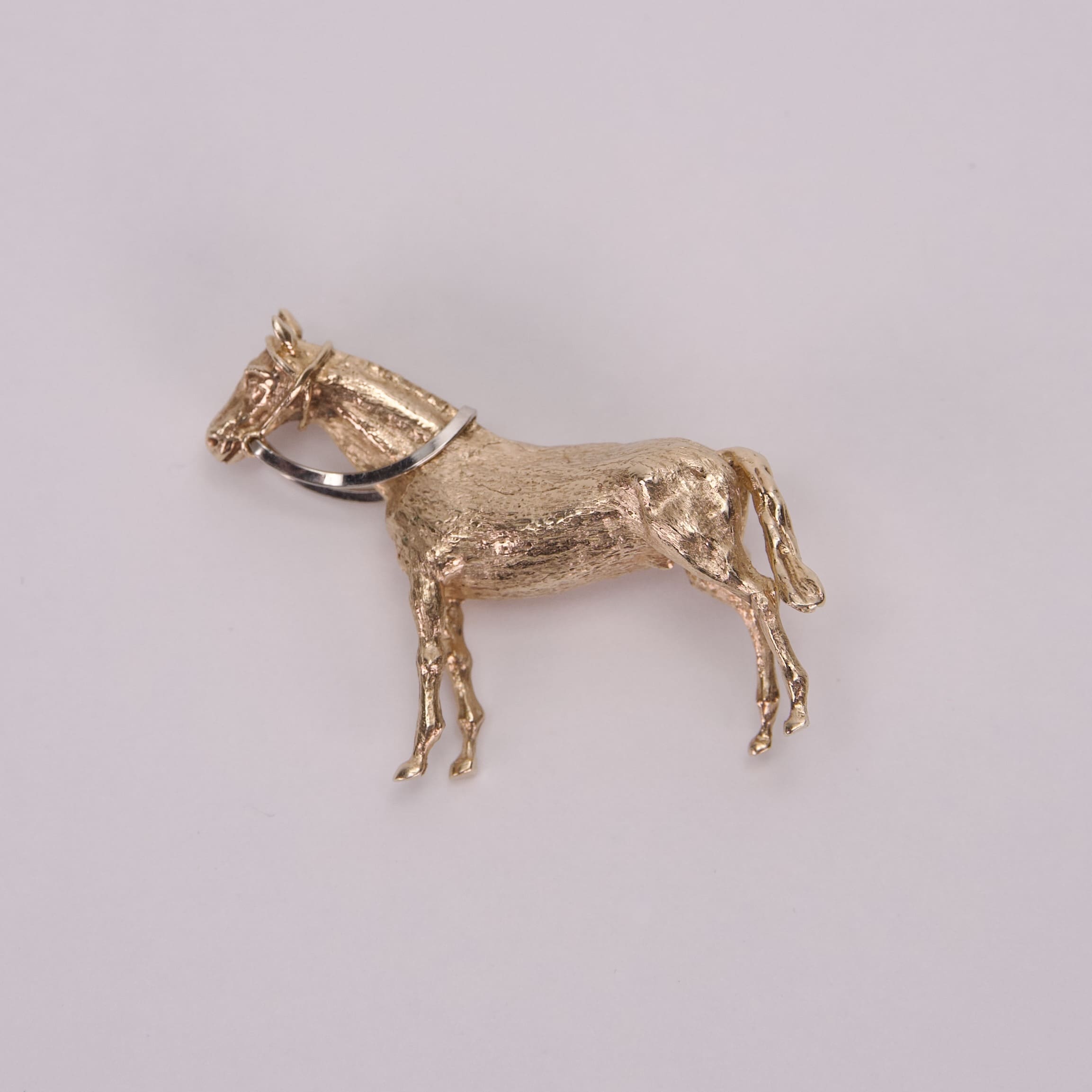Gold horse-shaped brooch on white background.