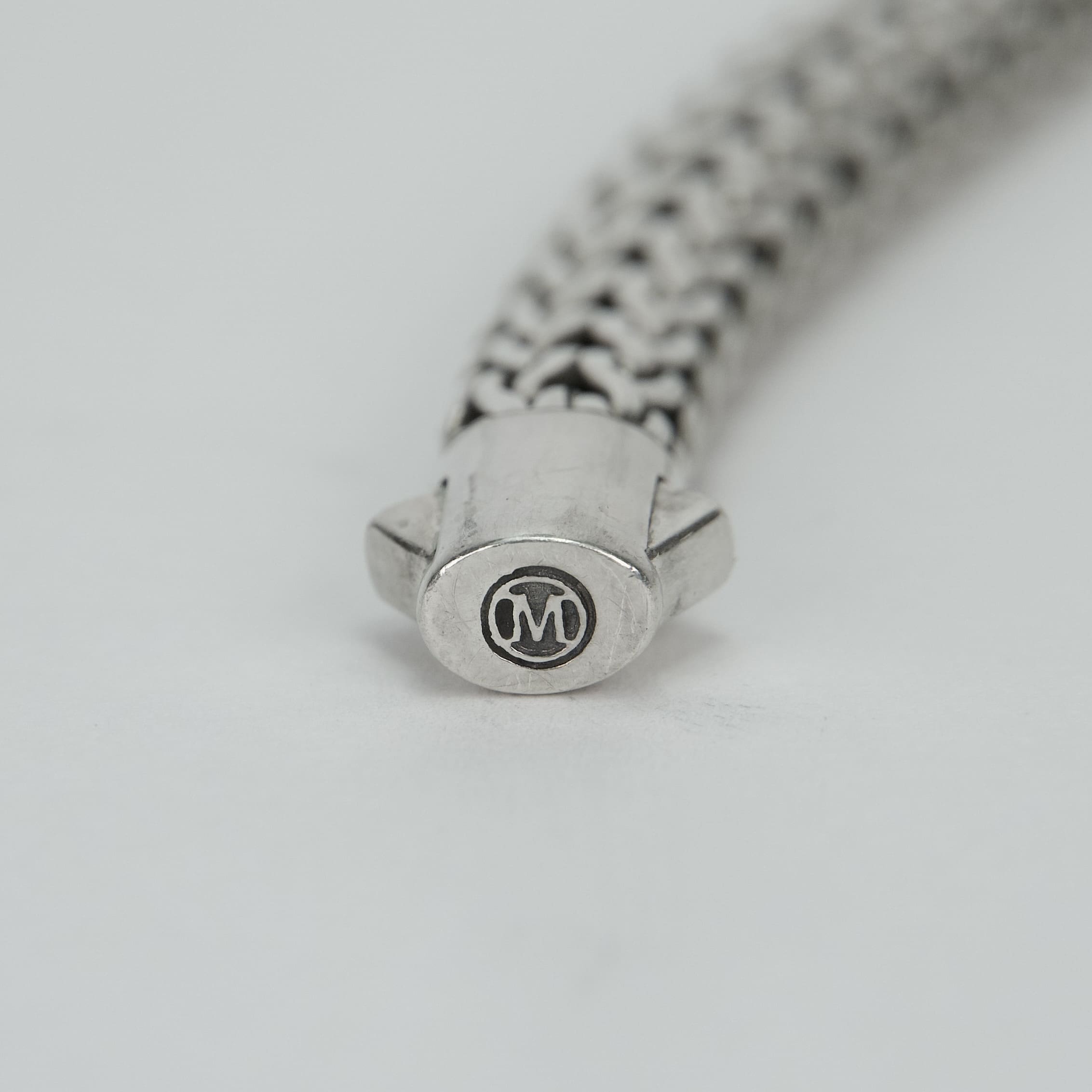 Silver bracelet clasp with engraved "M" logo.