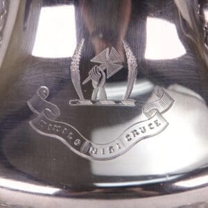 Engraved silver item with emblem and motto.