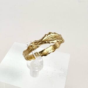 Ornate gold ring on clear display stand.