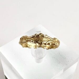 Ornate gold ring on clear display stand.