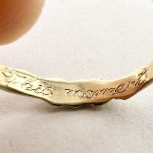 Engraved gold ring with "This moment" text.