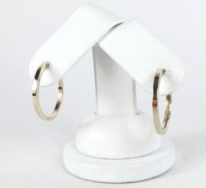 Gold hoop earrings on white display stand.